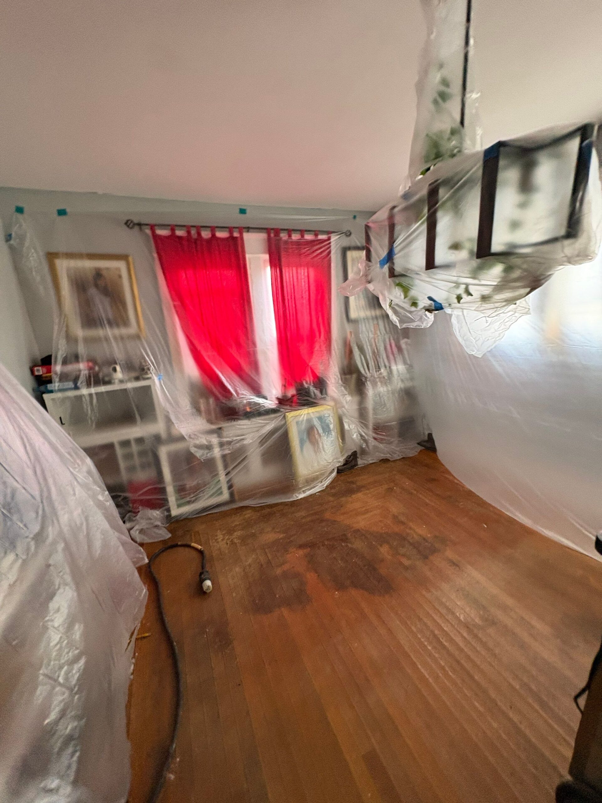 Buckled and moisture-stained historic hardwood floors in Easton PA living room under plastic containment during pipe burst water damage restoration